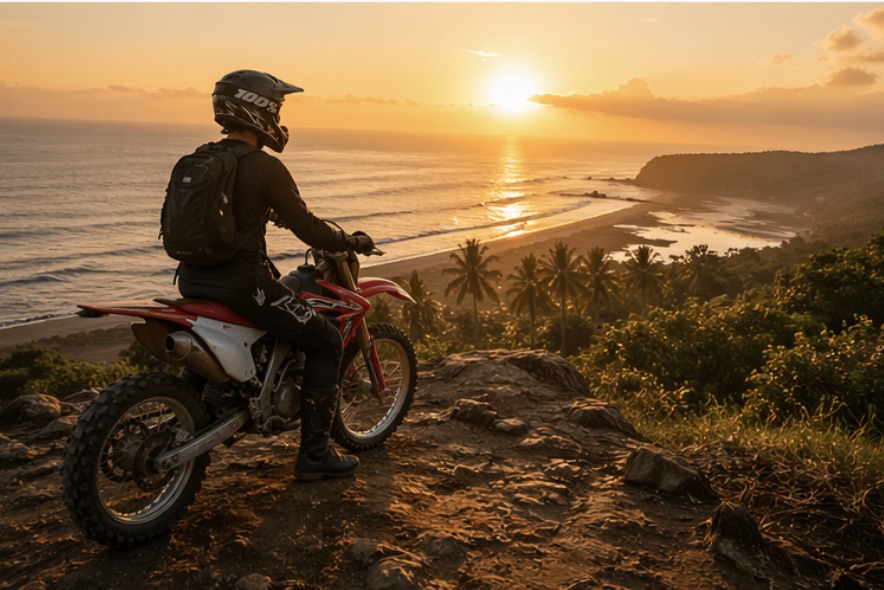 Rider on red CRF dirt bike parked on a cliffside at sunset, watching the sun melt into the Pacific ocean